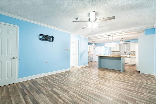 unfurnished living room featuring sink, a textured ceiling, light wood-type flooring, ornamental molding, and ceiling fan