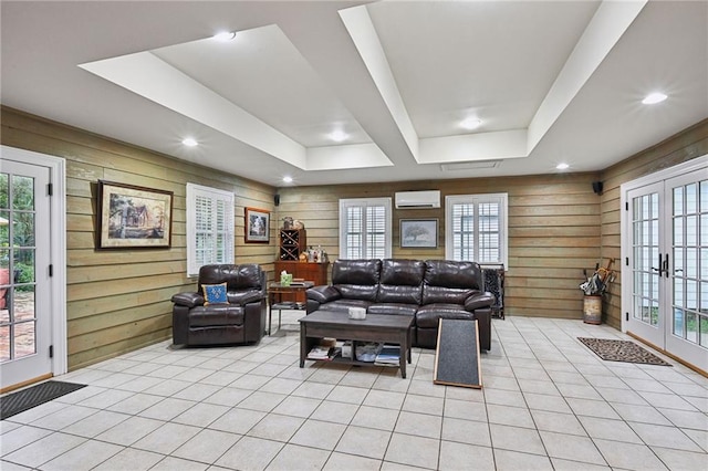 living room featuring a tray ceiling, french doors, and wood walls