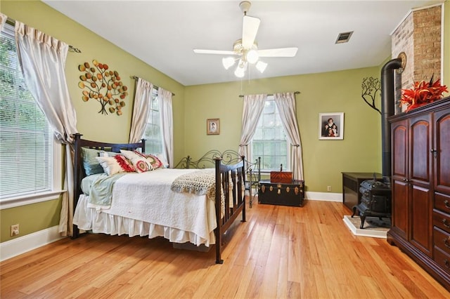 bedroom featuring a wood stove, light hardwood / wood-style flooring, and ceiling fan