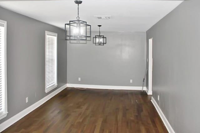 unfurnished dining area with a wealth of natural light, dark hardwood / wood-style floors, and an inviting chandelier