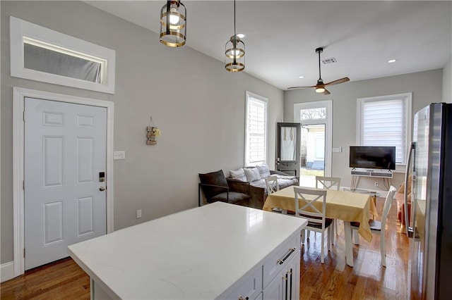 kitchen featuring stainless steel fridge, decorative light fixtures, a center island, ceiling fan, and dark wood-type flooring