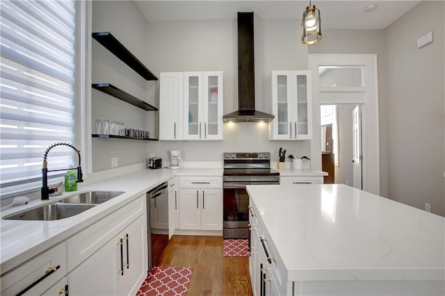 kitchen featuring pendant lighting, white cabinetry, sink, appliances with stainless steel finishes, and wall chimney range hood