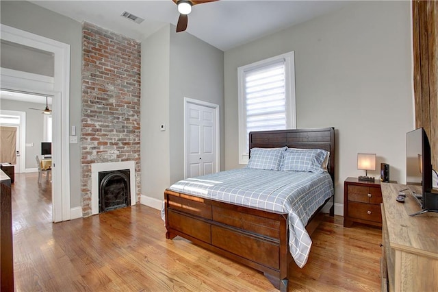 bedroom with a large fireplace, ceiling fan, a closet, and light wood-type flooring