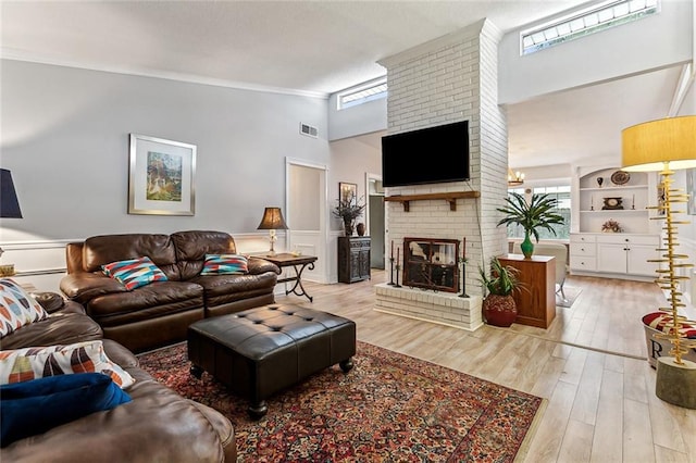 living room with ornamental molding, a brick fireplace, plenty of natural light, and light hardwood / wood-style flooring