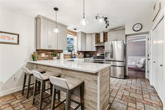 kitchen featuring appliances with stainless steel finishes, kitchen peninsula, a kitchen bar, and wall chimney exhaust hood