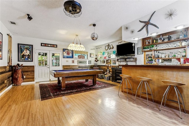 game room with light hardwood / wood-style flooring, bar area, a textured ceiling, and french doors