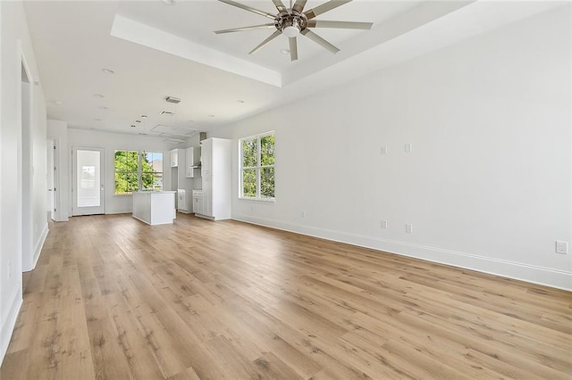 unfurnished living room featuring light hardwood / wood-style flooring, a tray ceiling, and ceiling fan