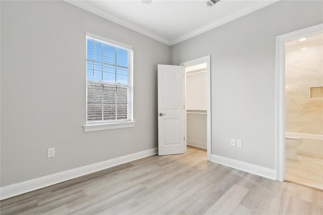 unfurnished bedroom featuring ornamental molding, light hardwood / wood-style flooring, ensuite bathroom, and a walk in closet