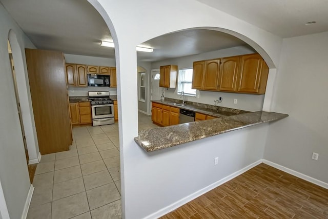 kitchen with kitchen peninsula, sink, light hardwood / wood-style flooring, appliances with stainless steel finishes, and dark stone counters