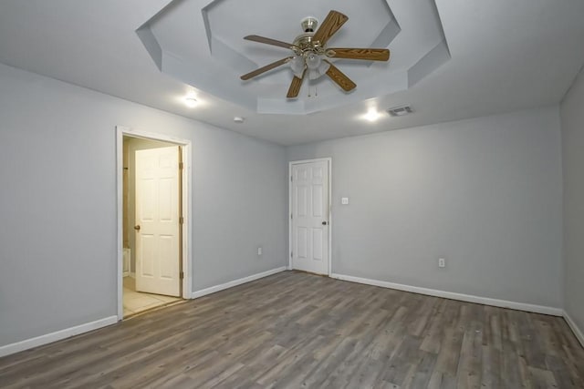 empty room featuring a raised ceiling, dark hardwood / wood-style floors, and ceiling fan