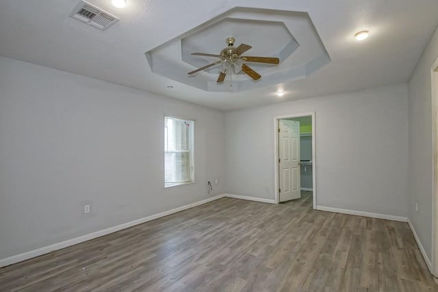 empty room featuring a tray ceiling, light wood-type flooring, and ceiling fan