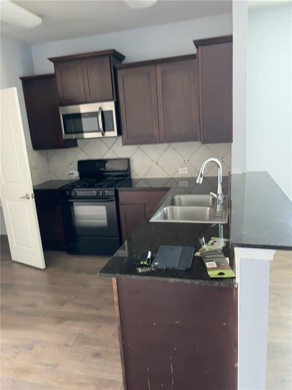 kitchen featuring light hardwood / wood-style floors, black gas range oven, tasteful backsplash, kitchen peninsula, and sink