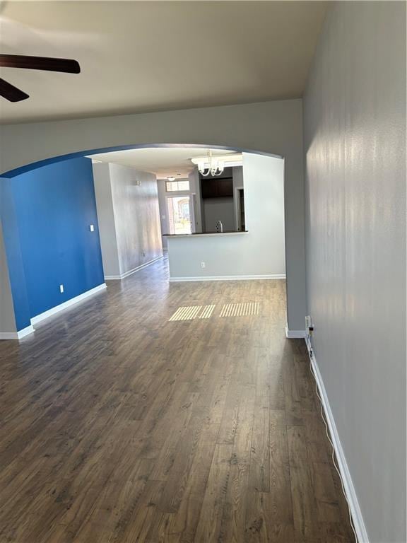 unfurnished living room with ceiling fan with notable chandelier and dark wood-type flooring