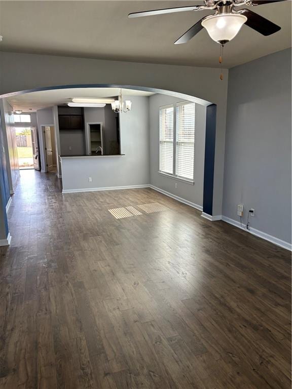 unfurnished living room featuring ceiling fan with notable chandelier, dark wood-type flooring, and a wealth of natural light