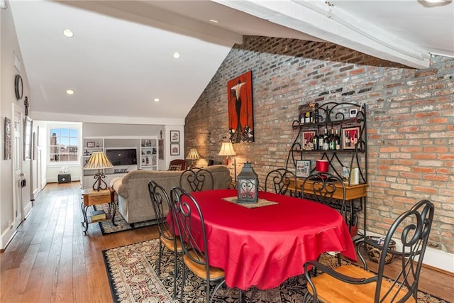 dining area featuring wood-type flooring, brick wall, and vaulted ceiling with beams