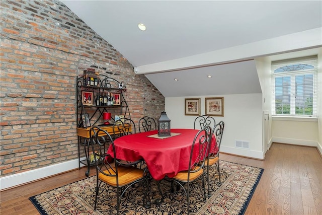 dining area with lofted ceiling, light hardwood / wood-style flooring, and brick wall