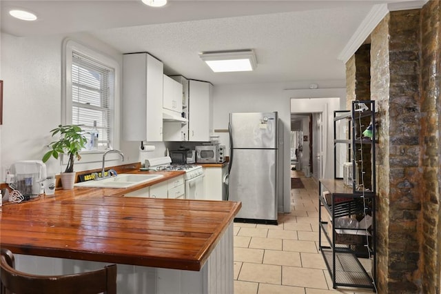 kitchen featuring appliances with stainless steel finishes, white cabinetry, kitchen peninsula, wooden counters, and sink