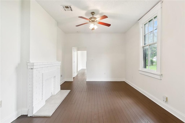 empty room with a fireplace, dark wood-type flooring, and ceiling fan