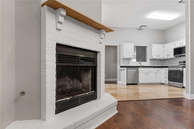 kitchen with sink, white cabinetry, a brick fireplace, appliances with stainless steel finishes, and hardwood / wood-style floors