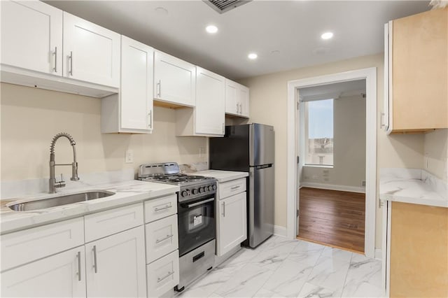 kitchen featuring white cabinetry, sink, light stone countertops, appliances with stainless steel finishes, and light hardwood / wood-style floors