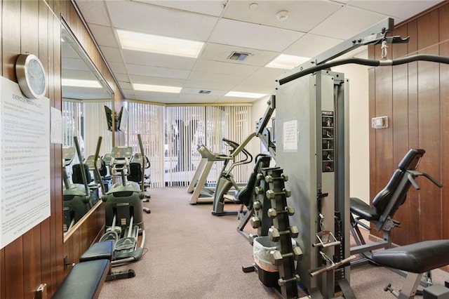 exercise room with a paneled ceiling, carpet, and wood walls