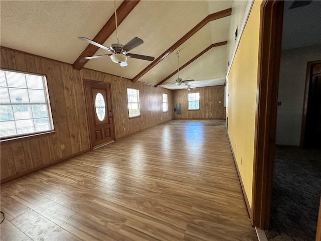 entryway with lofted ceiling with beams, a wealth of natural light, and wood walls