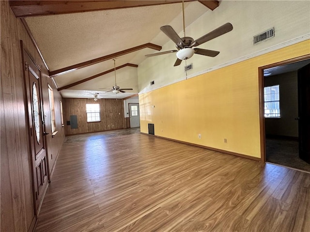 unfurnished living room featuring wood walls, wood-type flooring, vaulted ceiling with beams, a textured ceiling, and ceiling fan