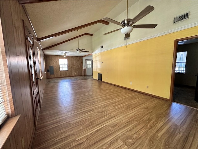 unfurnished living room featuring vaulted ceiling with beams, wood walls, hardwood / wood-style flooring, and plenty of natural light