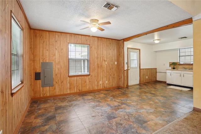 unfurnished room featuring electric panel, ceiling fan, a textured ceiling, and wooden walls