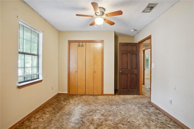 unfurnished bedroom featuring light carpet, a closet, a textured ceiling, and ceiling fan