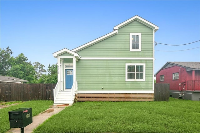 rear view of house with entry steps, a yard, and fence