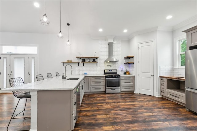 kitchen with gray cabinets, a sink, open shelves, stainless steel appliances, and wall chimney exhaust hood