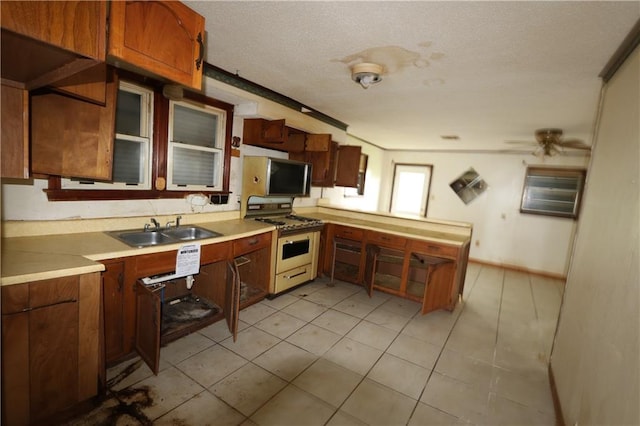 kitchen featuring gas stove, sink, light tile patterned flooring, ceiling fan, and a textured ceiling