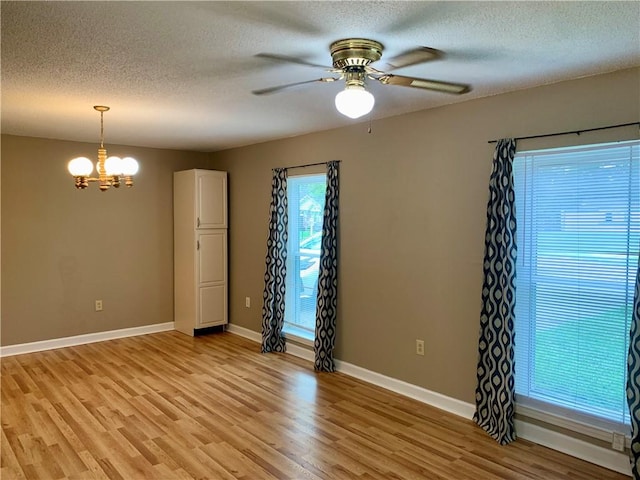 empty room with a textured ceiling, ceiling fan with notable chandelier, and light wood-type flooring