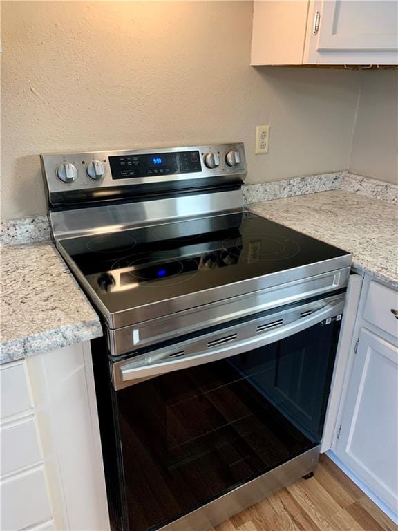 kitchen featuring stainless steel electric range, white cabinets, and light hardwood / wood-style floors