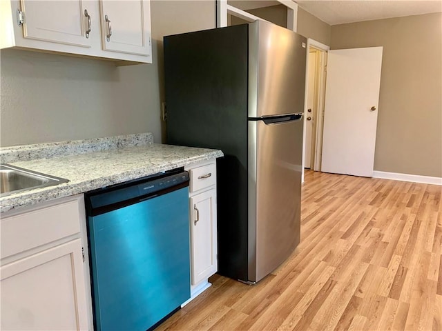 kitchen with dishwasher, stainless steel fridge, white cabinets, light stone countertops, and light wood-type flooring