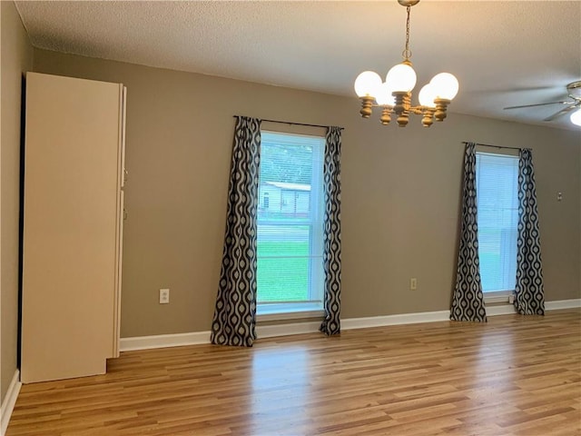 empty room featuring ceiling fan with notable chandelier, light hardwood / wood-style flooring, and a textured ceiling