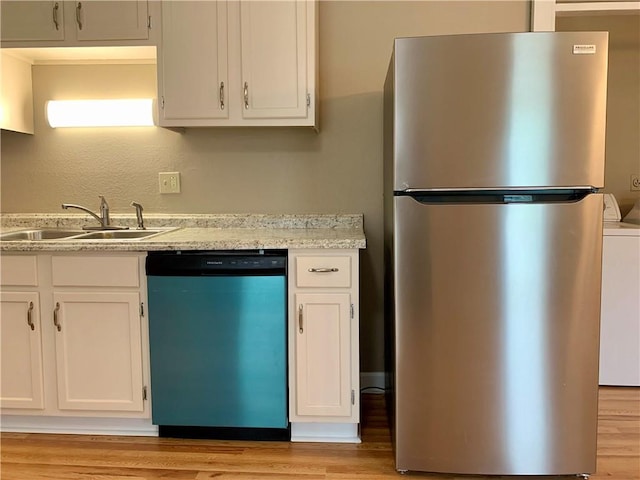 kitchen with light wood-type flooring, appliances with stainless steel finishes, white cabinetry, sink, and washer / dryer