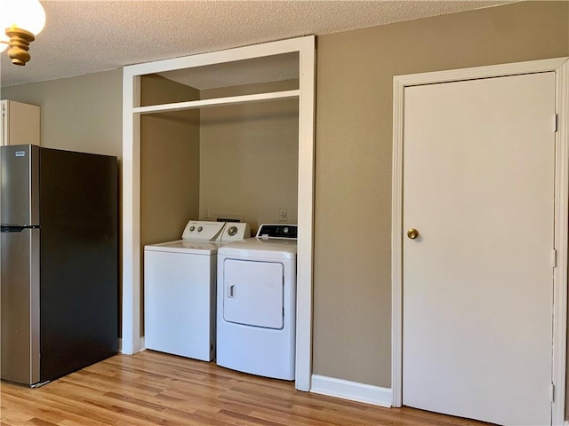 clothes washing area with a textured ceiling, light hardwood / wood-style flooring, and washer and clothes dryer