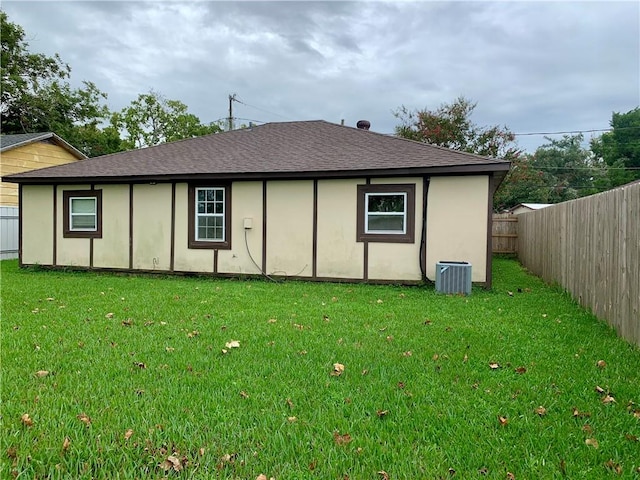 rear view of property with central air condition unit and a lawn