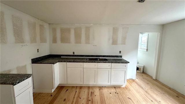 kitchen with light hardwood / wood-style flooring, white cabinets, dark stone countertops, and sink