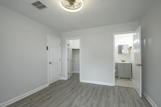 unfurnished bedroom with ensuite bath, hardwood / wood-style floors, sink, a closet, and a spacious closet