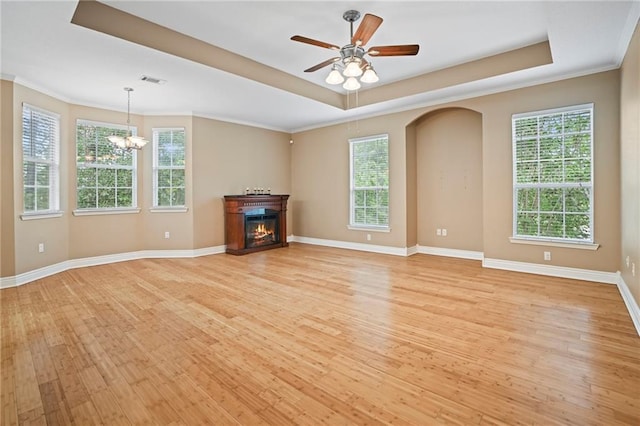 unfurnished living room featuring a healthy amount of sunlight, ceiling fan with notable chandelier, a raised ceiling, and light hardwood / wood-style flooring