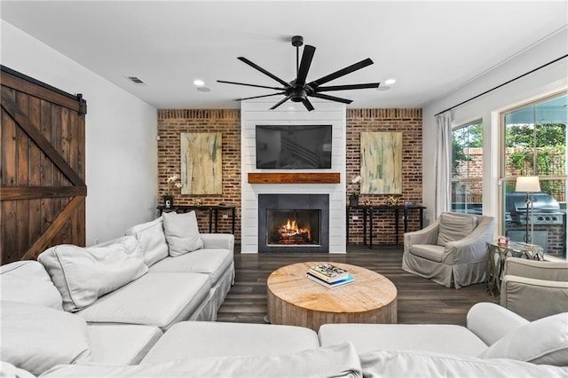 living room featuring a fireplace, ceiling fan, dark hardwood / wood-style floors, brick wall, and a barn door