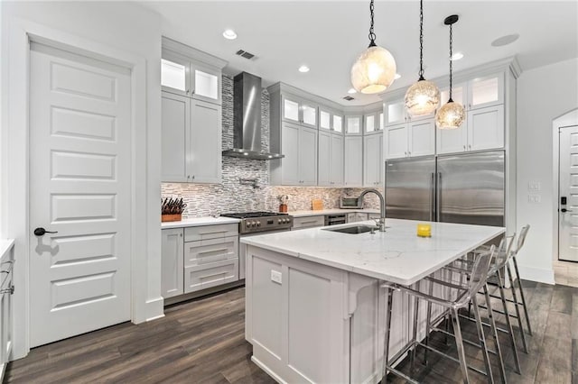 kitchen with built in fridge, dark hardwood / wood-style floors, decorative light fixtures, wall chimney exhaust hood, and sink