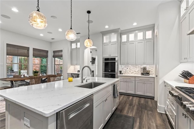 kitchen with decorative light fixtures, dark hardwood / wood-style flooring, sink, appliances with stainless steel finishes, and a center island with sink