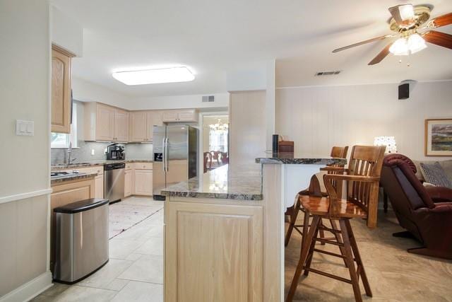 kitchen with light brown cabinetry, stainless steel appliances, sink, ceiling fan, and dark stone countertops