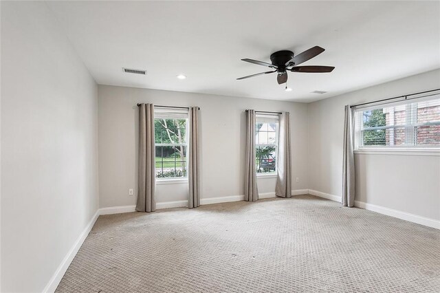 empty room featuring a wealth of natural light, ceiling fan, and light carpet