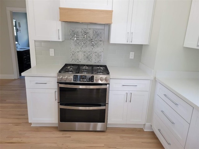 kitchen featuring light wood finished floors, range with two ovens, light countertops, white cabinetry, and tasteful backsplash