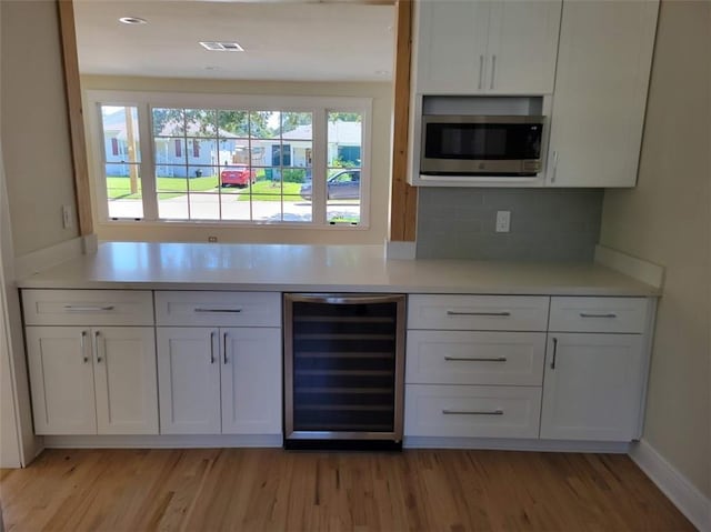 kitchen featuring stainless steel microwave, wine cooler, light wood-type flooring, light countertops, and white cabinets